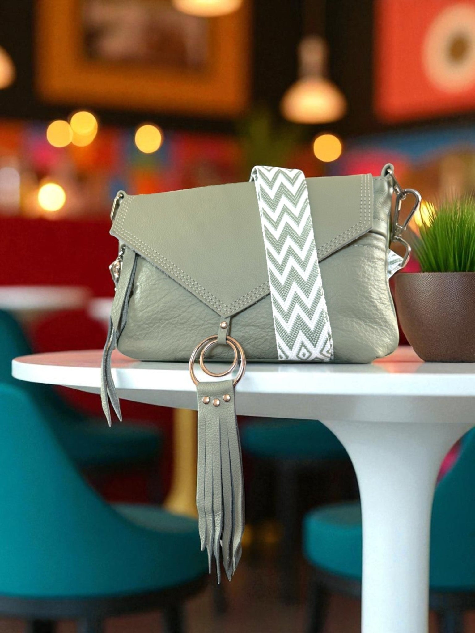 Light green handbag with a matching pale olive green and white chevron patterned, crossbody strap. on a white table in a colourful coffee shop setting. 
