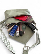 Light olive green leather handbag with various items including a red phone, cosmetics and sunglasses