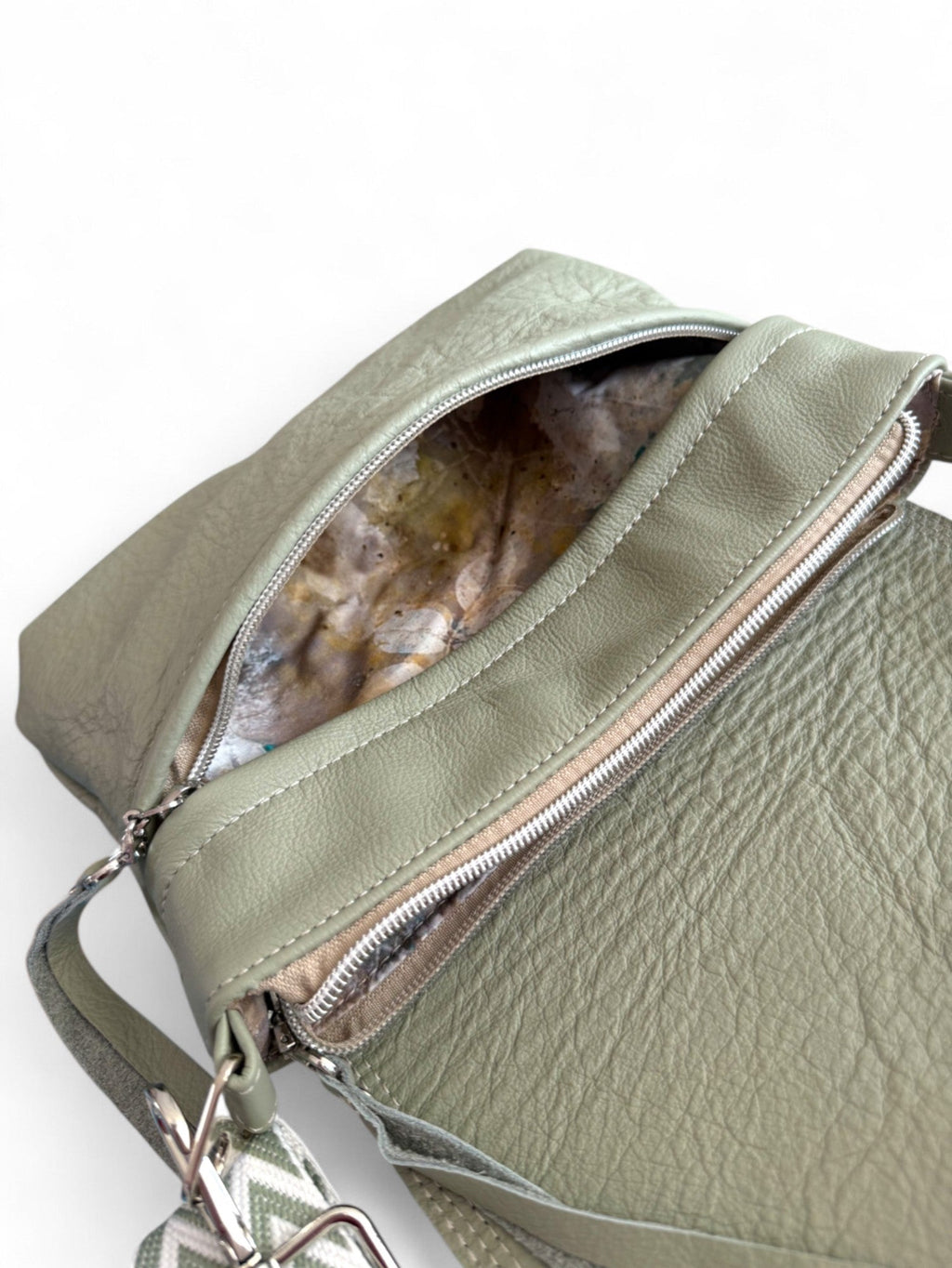 Light sage green leather handbag with an open front zippered pocket,showing the lining. 