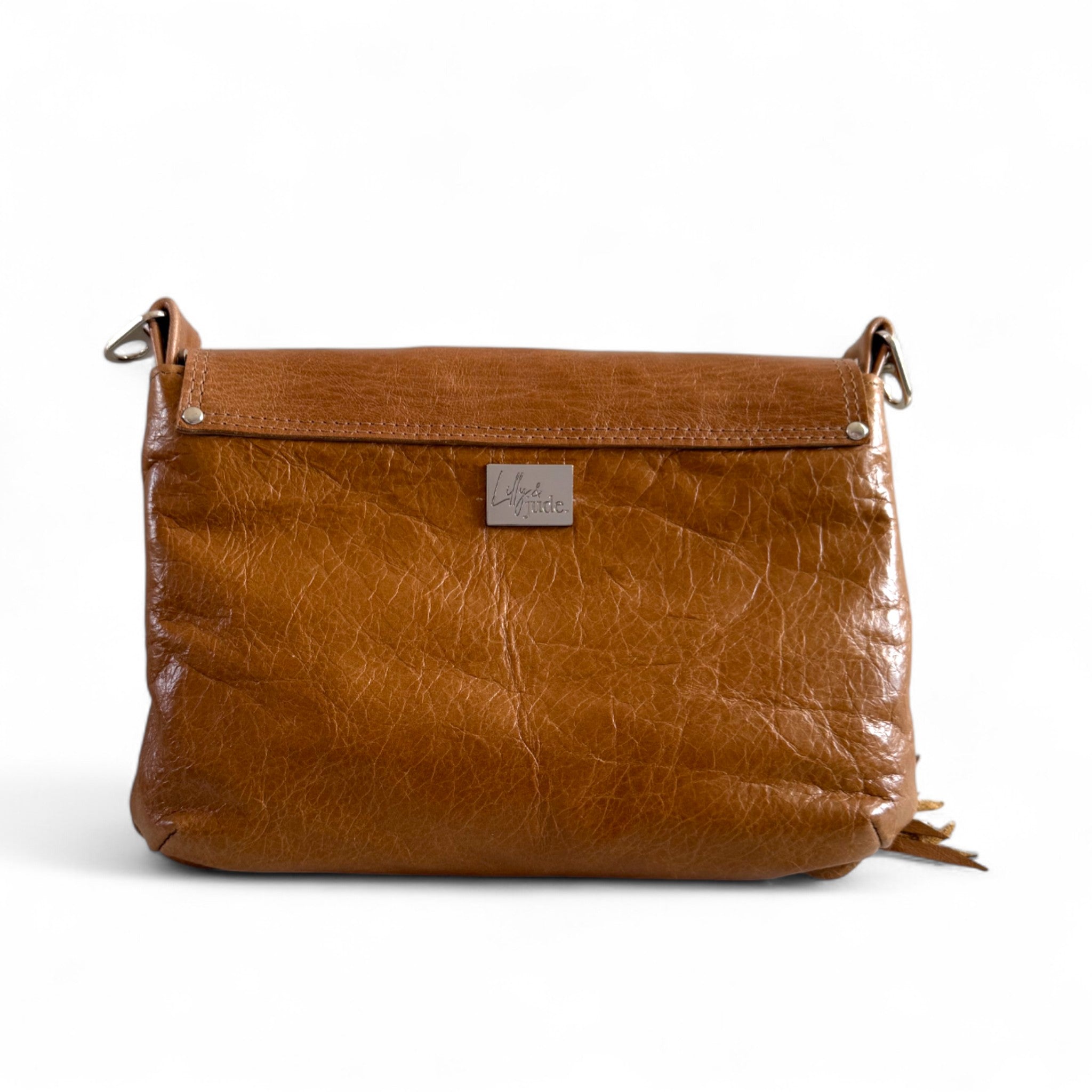 View of the back of a tan leather crossbody bag and focusses on the silver logo'd Lilly & Jude badge