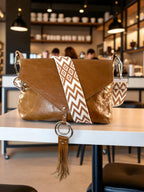 Tan brown handbag with a decorative strap on a table in a cafe setting. 