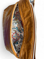 Slouchy crossbody bag, with the front zippered pocket  open to reveal the paisley patterned interior lining.