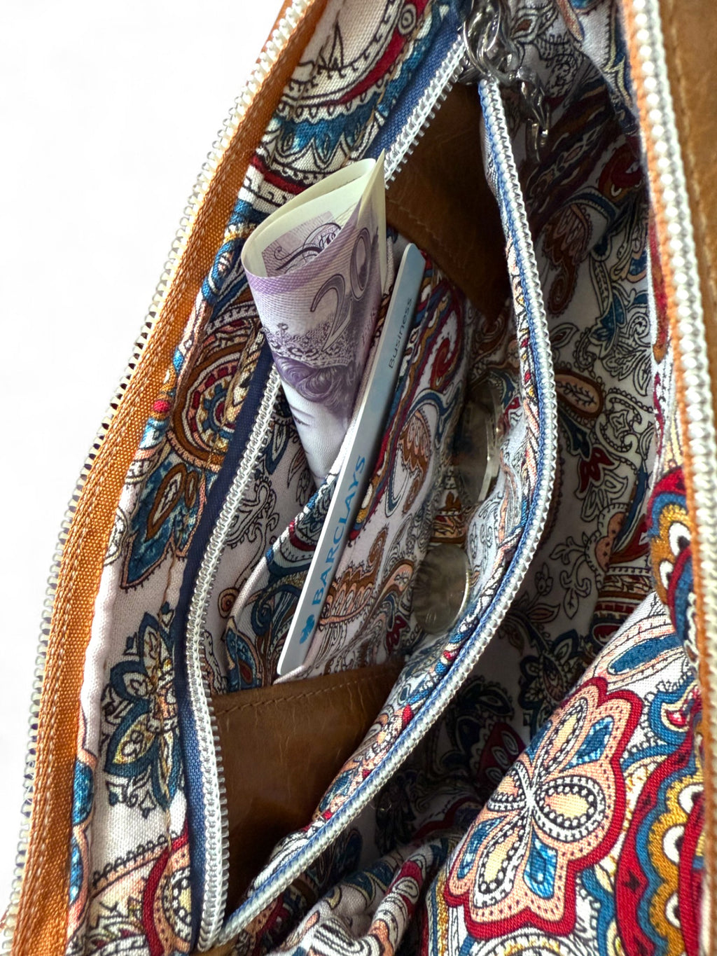 Inside view of the Olivia bag, showing the Paisley patterned lining, zipper pocket is open to reveal an integrated purse, containing cash, coins and bank card.