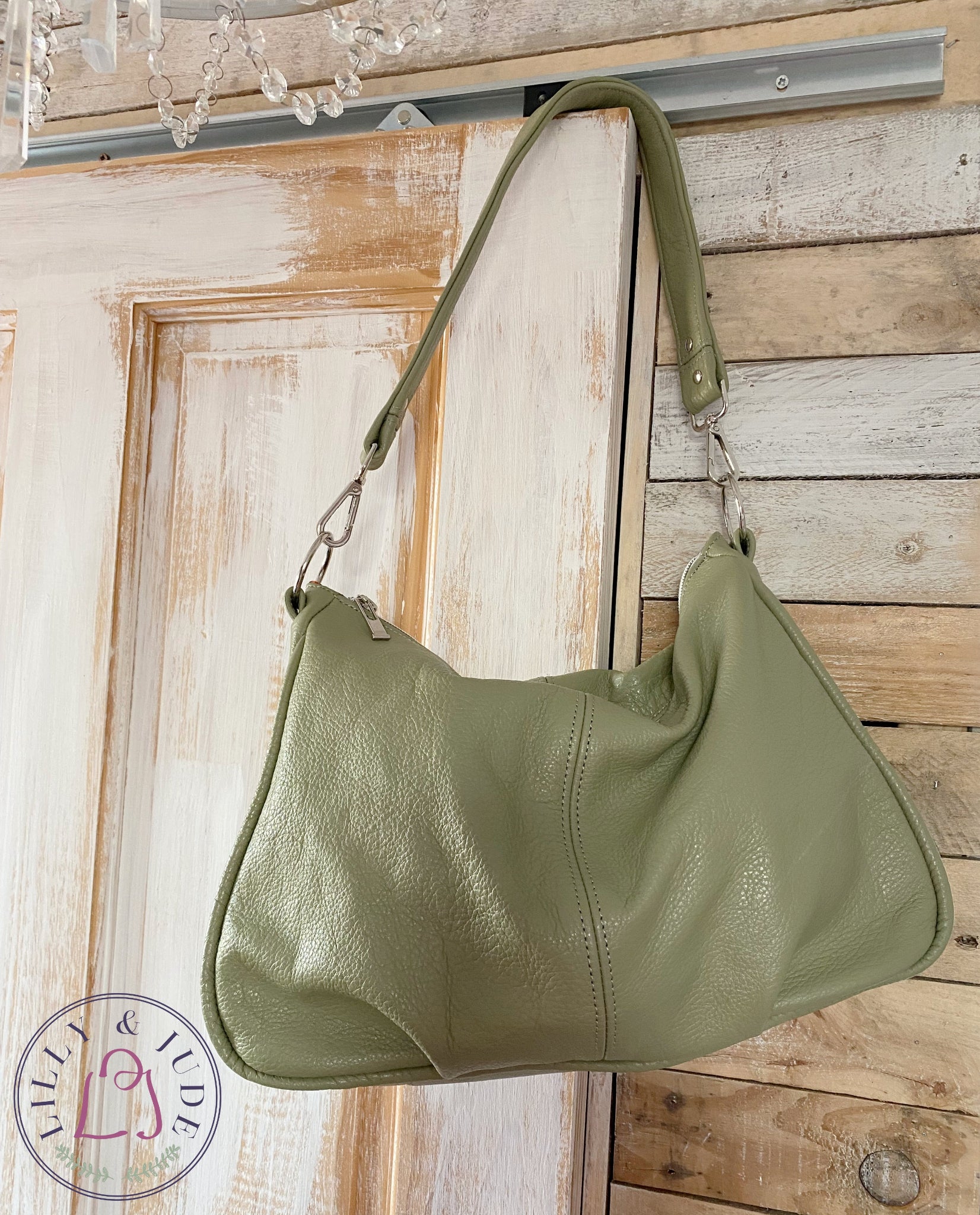 Sage green leather slouchy handbag hanging on a wooden door.