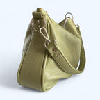 Side view of the soft sage green leather slouchy handbag with a strap on a white background