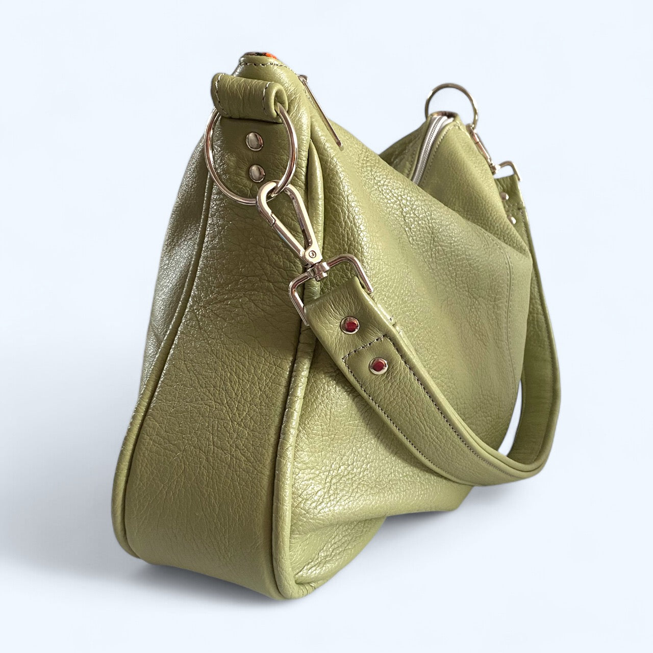 Side view of the soft sage green leather slouchy handbag with a strap on a white background