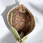 Open light green leather bag showing the interior lining fabric which is a mushroom brown coloured floral fabric on a neutral background