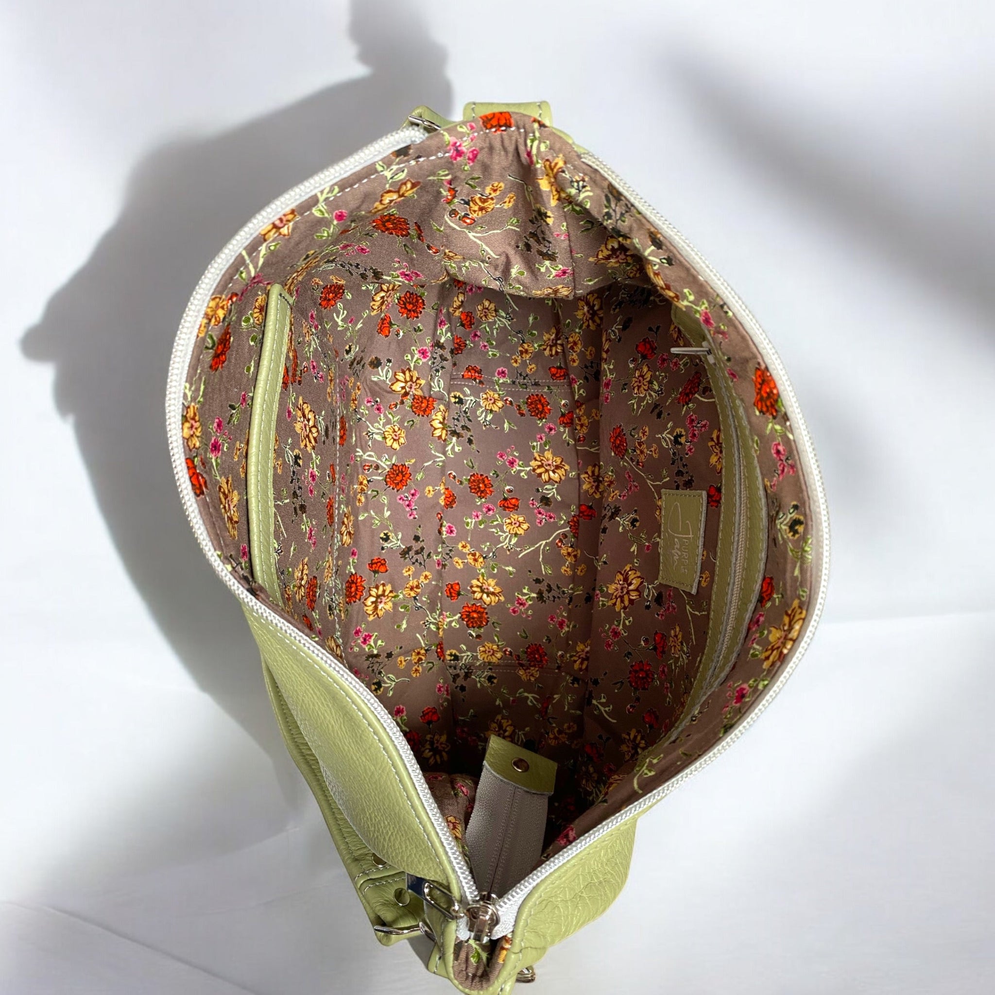 Open light green leather bag showing the interior lining fabric which is a mushroom brown coloured floral fabric on a neutral background