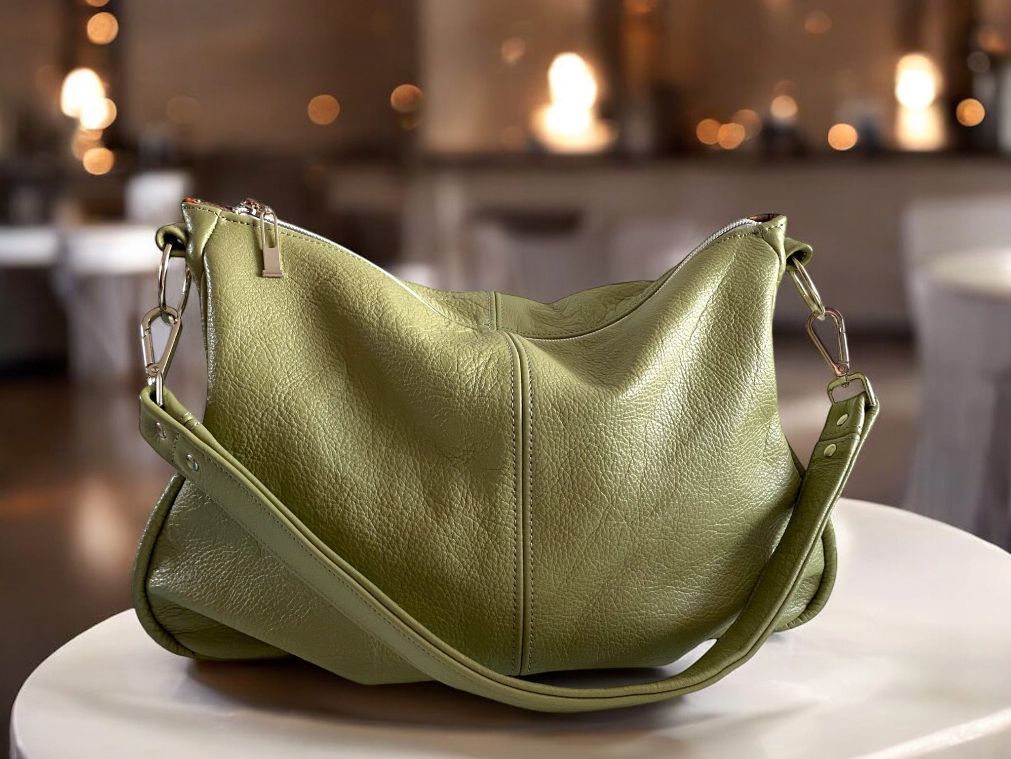 Pale green leather slouch handbag, with a leather strap and silver hardware on a white surface with blurred background