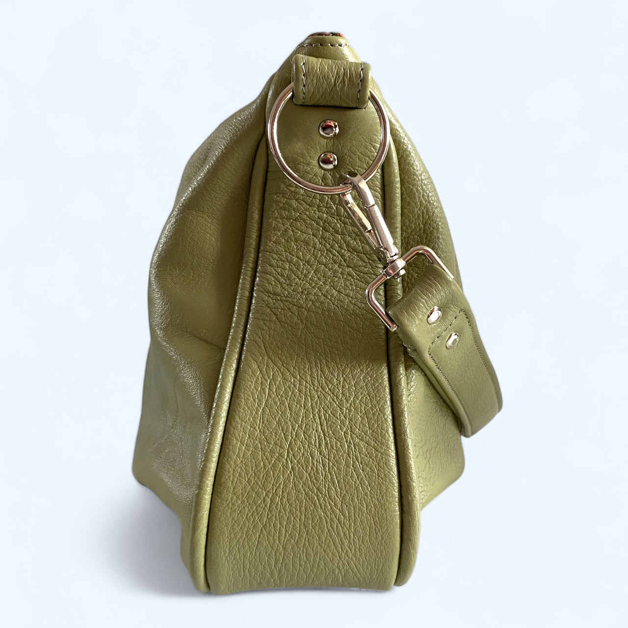 View of the side of a pale sage green leather handbag with silver circular strap connector hardware and leather strap, on a white background