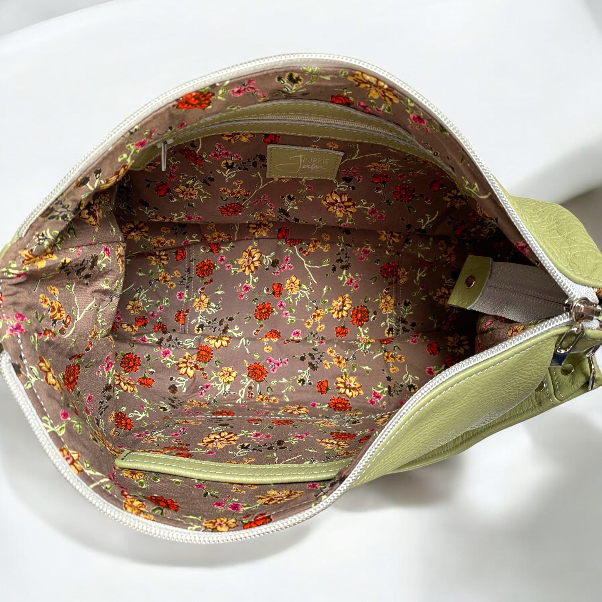 Birds Eye view of a pale green, real leather bag with its zip open to show the mushroom brown coloured, ditsy floral patterned lining fabric and the internal pockets 
