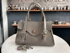 Grey leather handbag with silver hardware on a marble surface with a blurred cafe background.