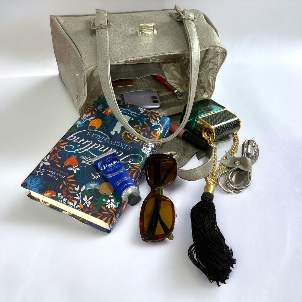 Collection of travel items including a book, sunglasses, and a leather bag on a white background