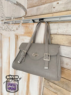 Grey leather handbag hanging on a wooden wall with a chandelier.