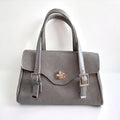 A grey leather handbag with an elegant silver twist lock, an adjustable leather straps on a white background.