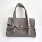 A grey leather handbag with an elegant silver twist lock, an adjustable leather straps on a white background.