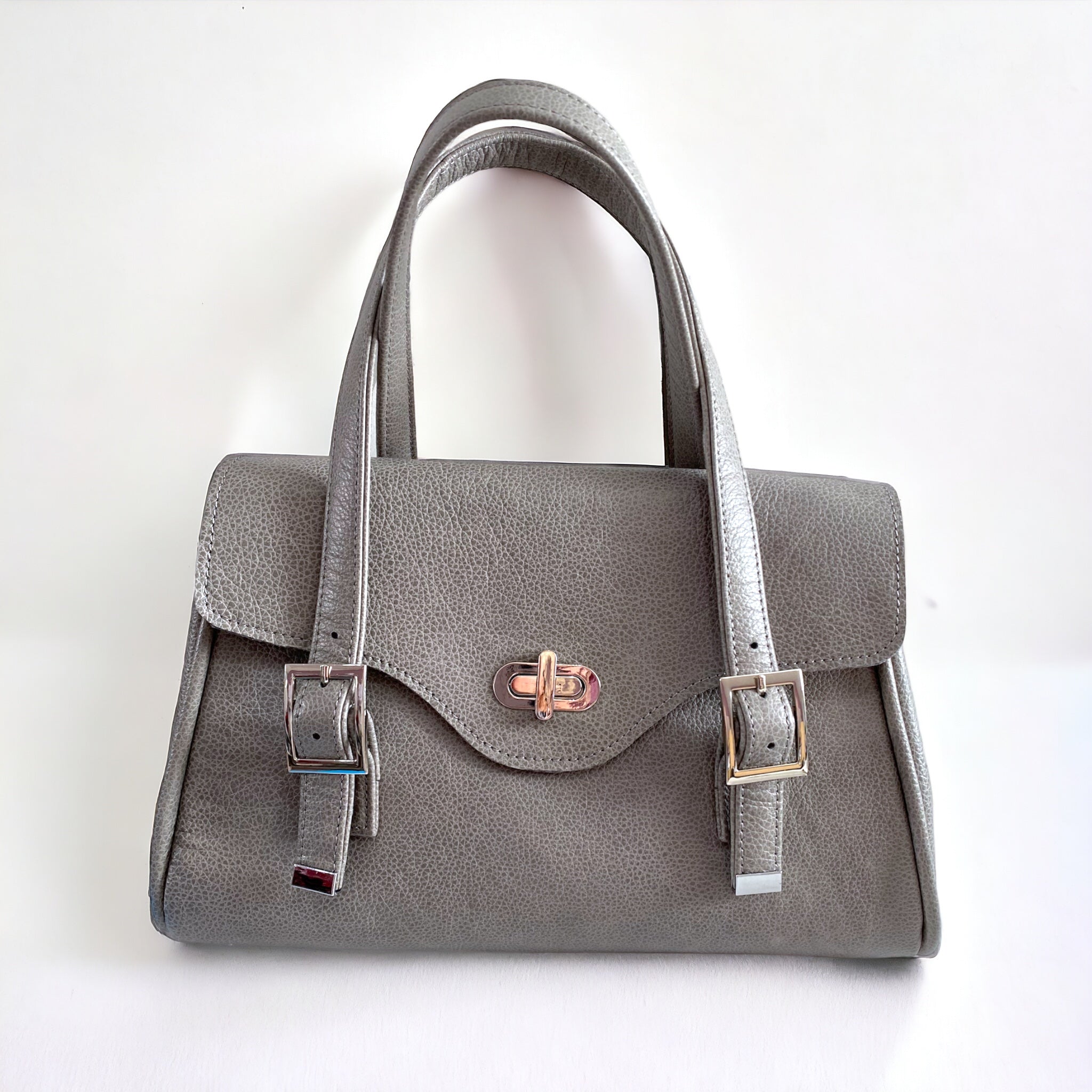 A grey leather handbag with an elegant silver twist lock, an adjustable leather straps on a white background.