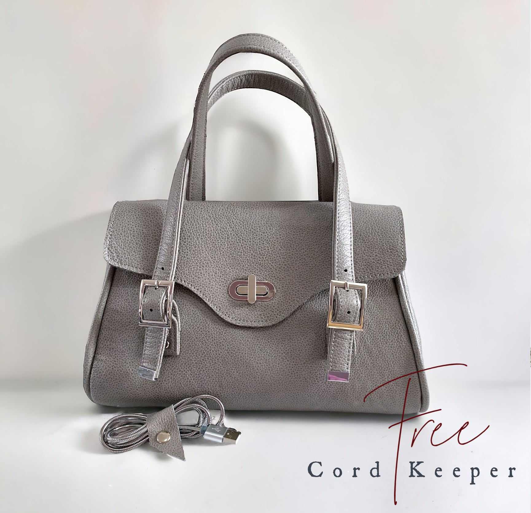 Grey leather handbag with USB cable and cord keeper on a white background