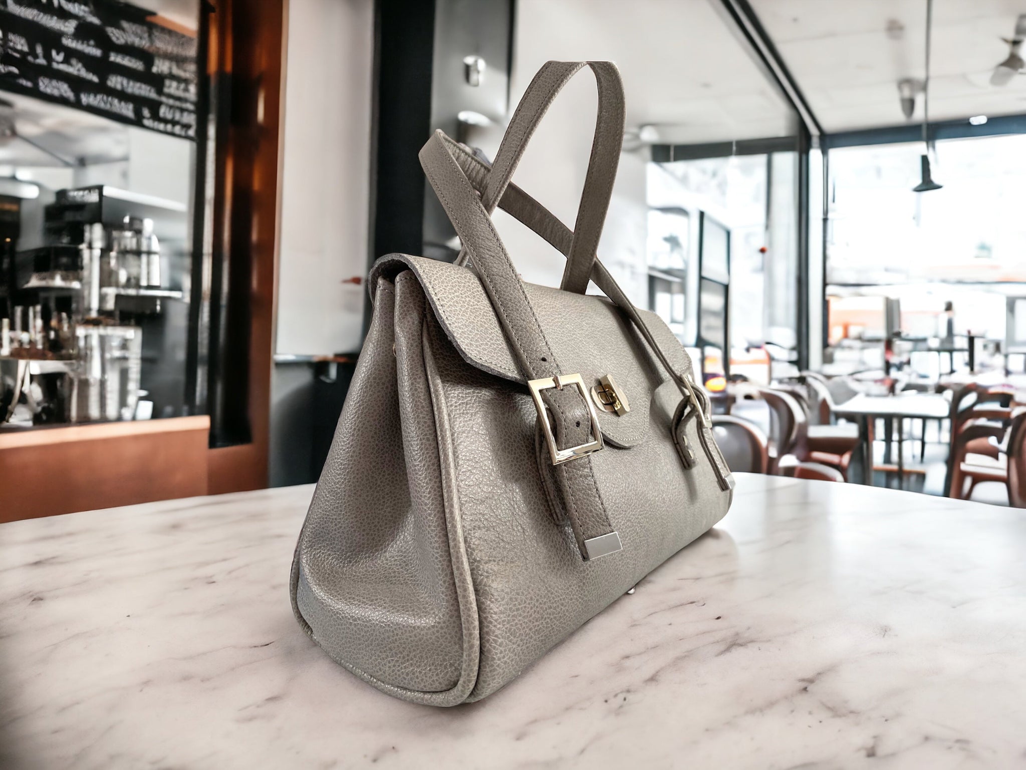 Grey rescued leather handbag with silver buckles and clasp on a coffee shop table