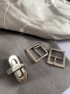 Silver metal buckles on a piece of the grey leather and silver coloured silk used to make the bag.
