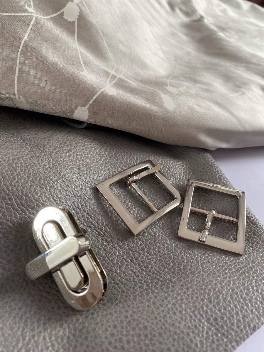 Silver metal buckles on a piece of the grey leather and silver coloured silk used to make the bag.