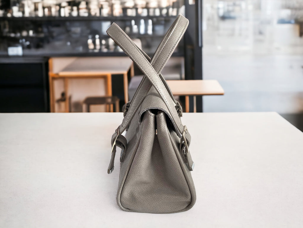 Side view of a grey, upcycled leather handbag on a white table with a blurred cafe background.