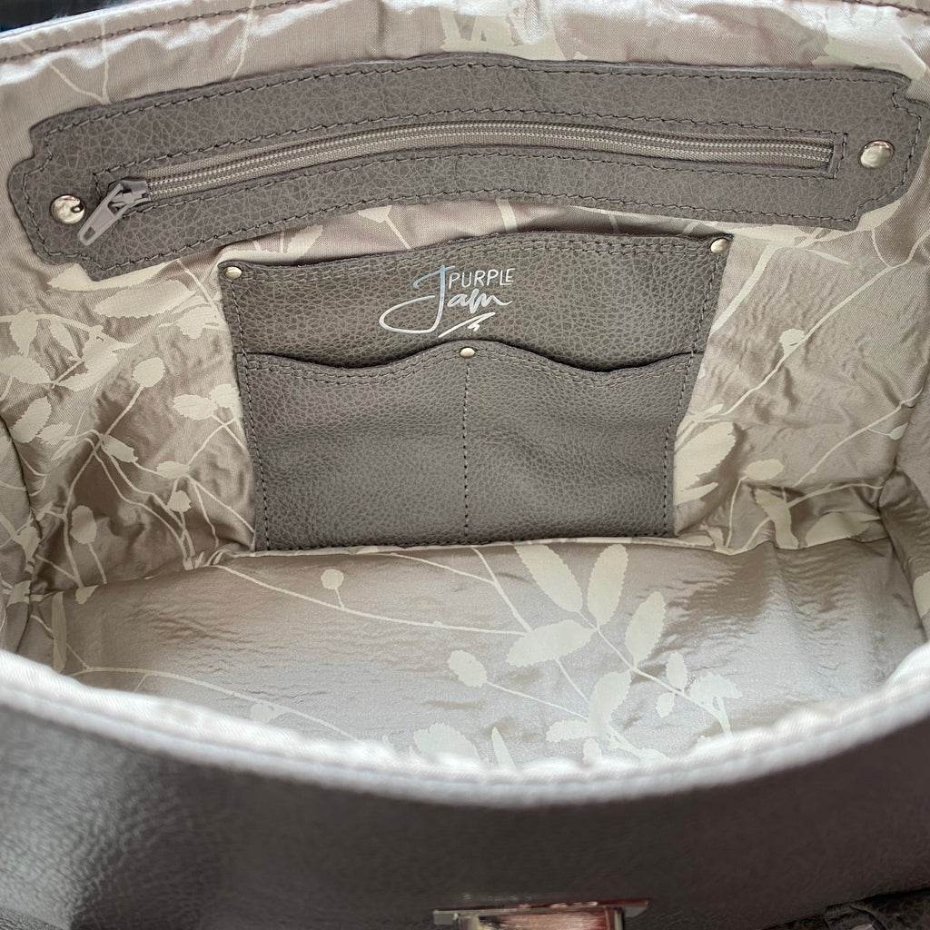 Interior view of a light grey leather handbag with silk interior slip pocket and Purple Jam logo 