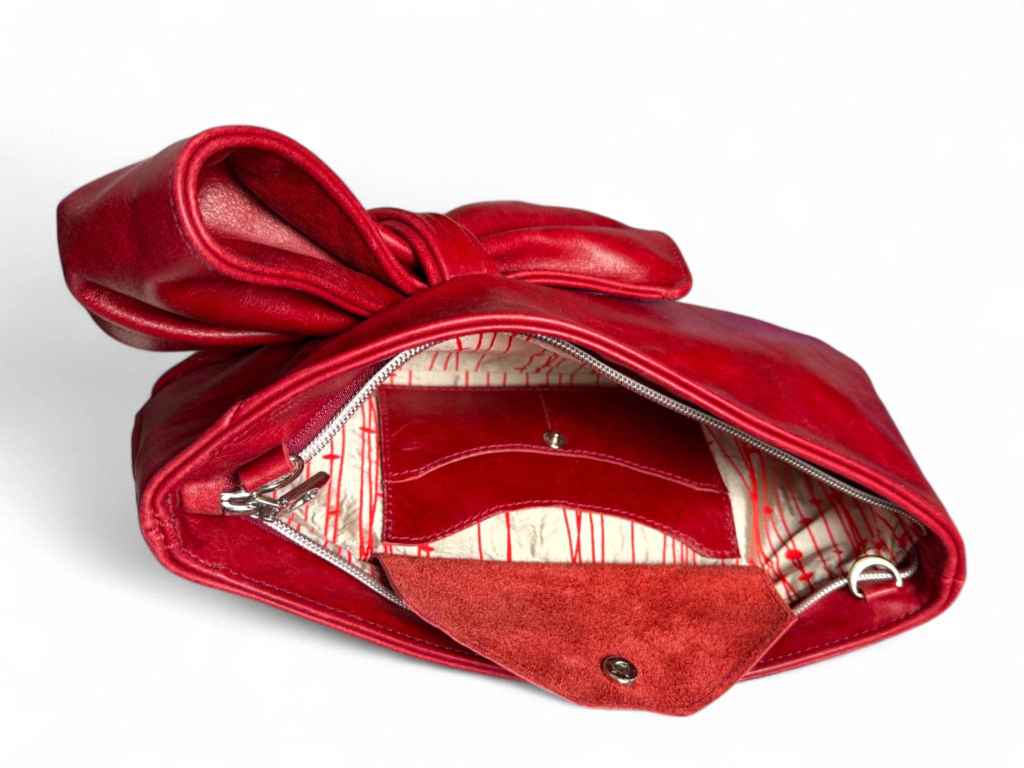 Red leather handbag with a bow on a white background. The image shows the silk interior lining and signature leather integrated purse