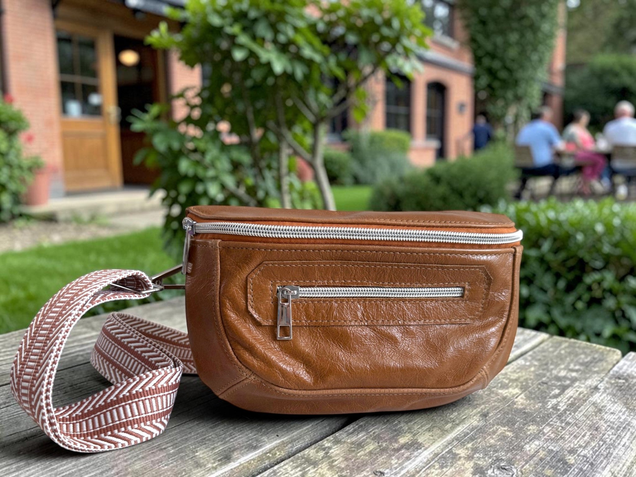 Tan brown leather, multiway bag with strap, sat on a wooden pub table in a beer garden