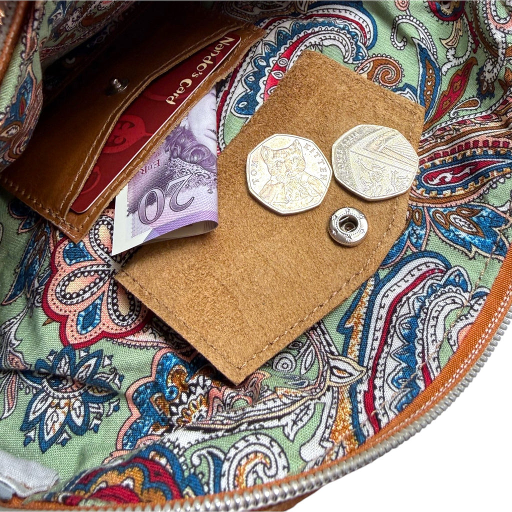 Close-up of the interior of a multiway bag, showing the patterned lining and integrated leather purse with a coin pouch containing coins, a card and a banknote.