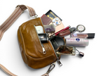 Tan brown leather bum bag, lying on a white background with various travel items and cosmetics, to show how spacious the bag is.