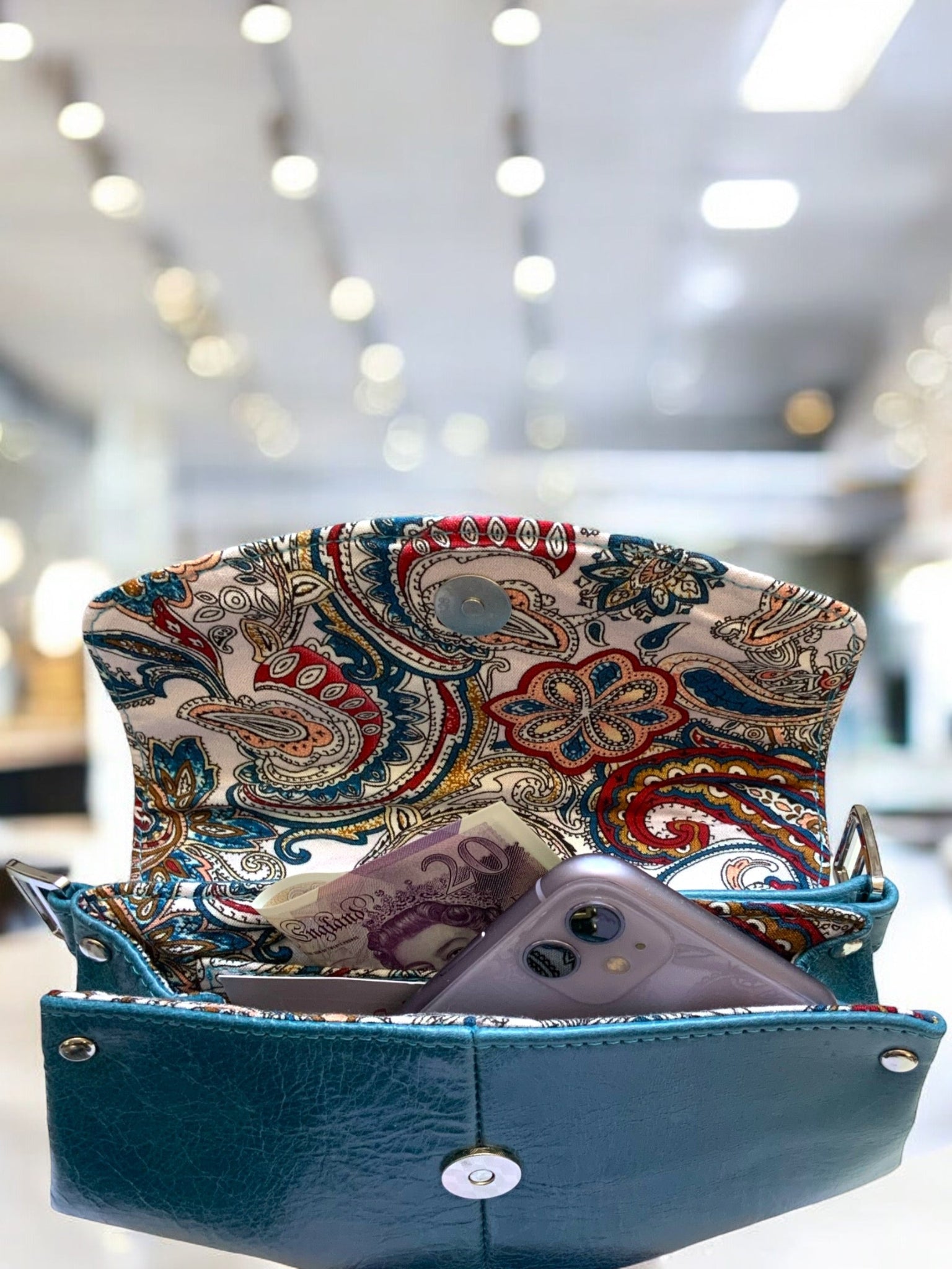 Purse with paisley flap and blue body, contents visible, blurred interior background