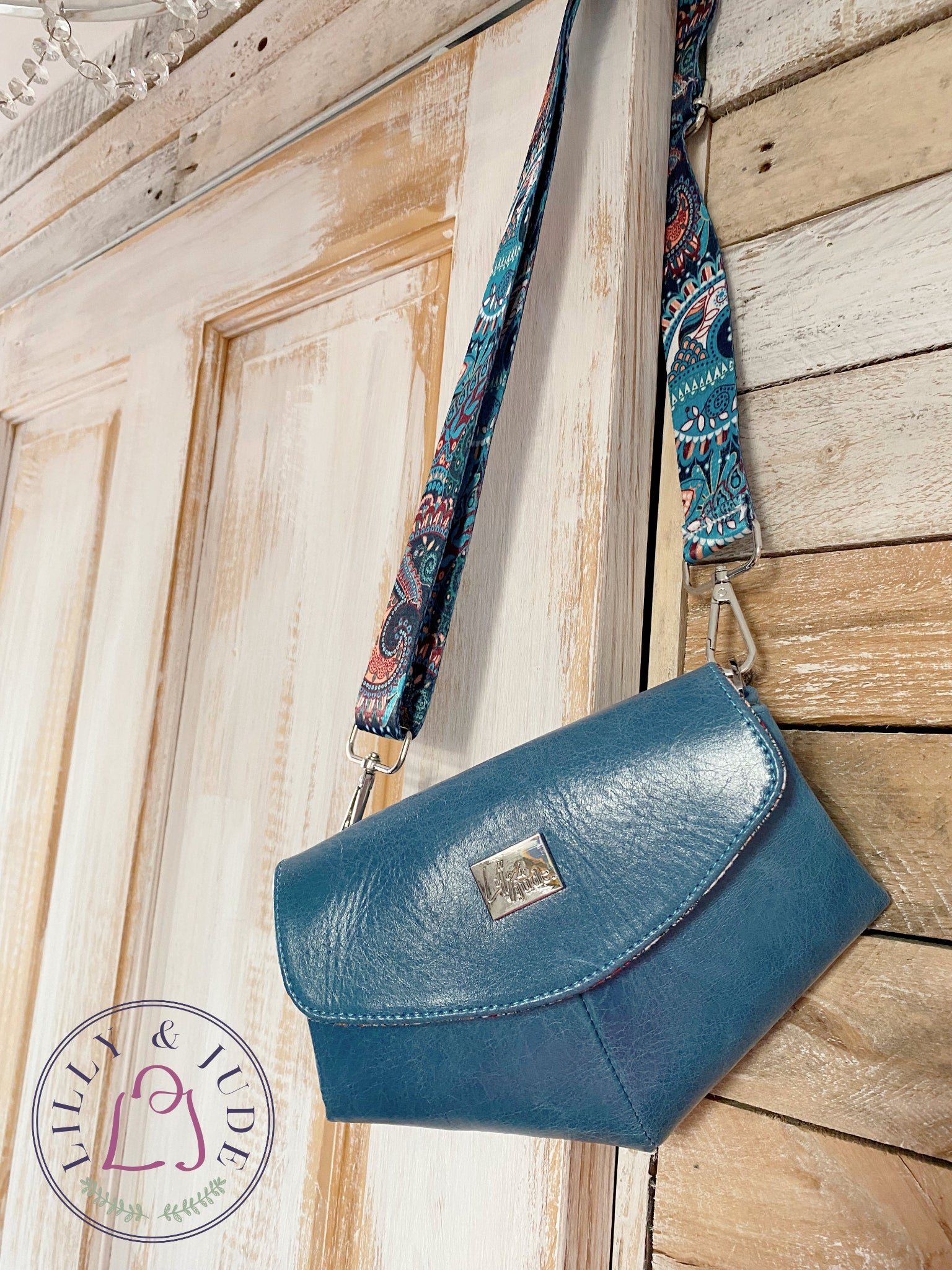 Blue handbag with patterned strap against a wooden background.