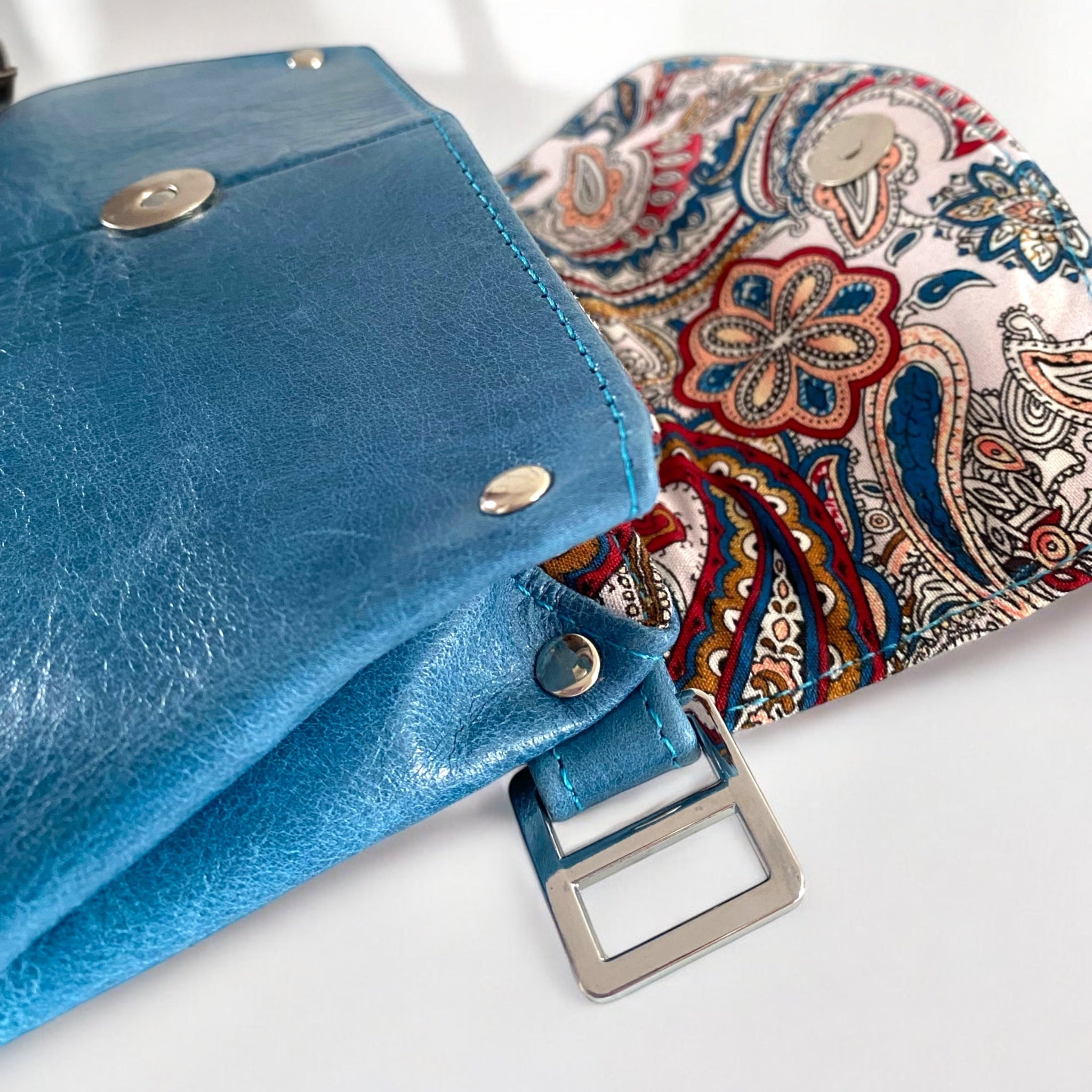 Blue leather bag with paisley fabric interior lining with silver hardwares on a white background