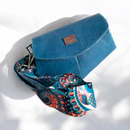Blue leather bag with a colorful paisley strap on a white background.