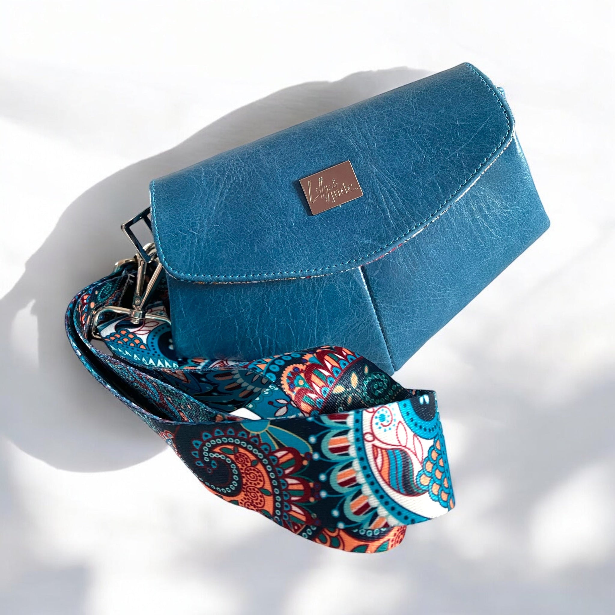Blue leather bag with a colorful paisley strap on a white background.