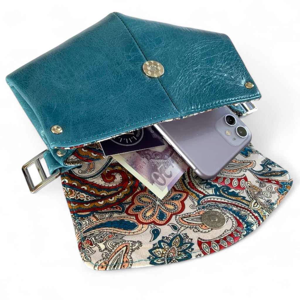 Bright blue leather clutch bag with paisley interior holding a phone and money.