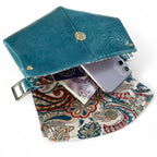 Bright blue leather clutch bag with paisley interior holding a phone and money.