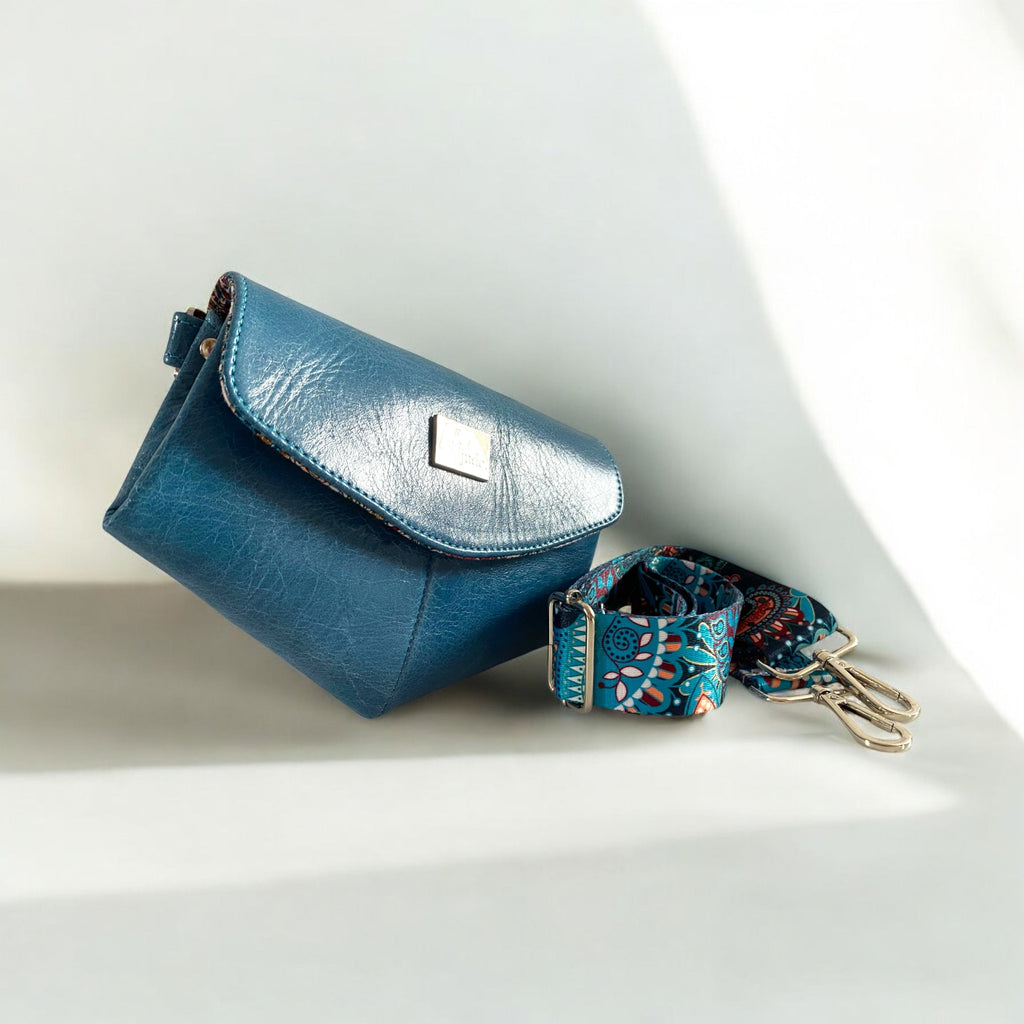 Unique shaped, blue, upcycled leather bag with paisley patterned strap on a light background