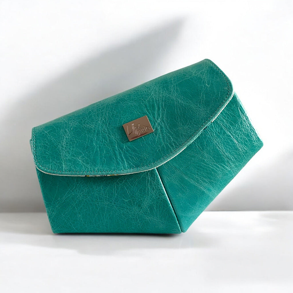 Unique shaped teal leather clutch bag with a textured surface on a white background.