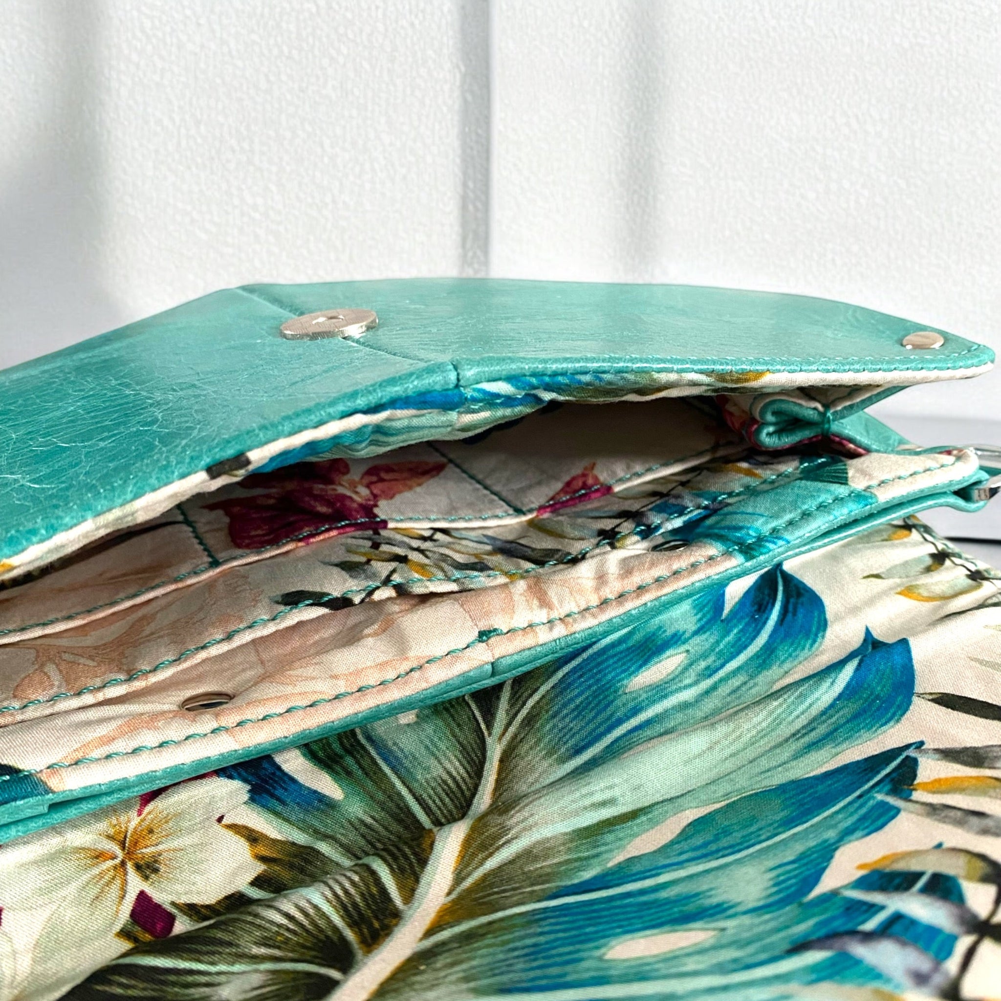 Floral-patterned fabric lining inside a turquoise leather crossbody bag.