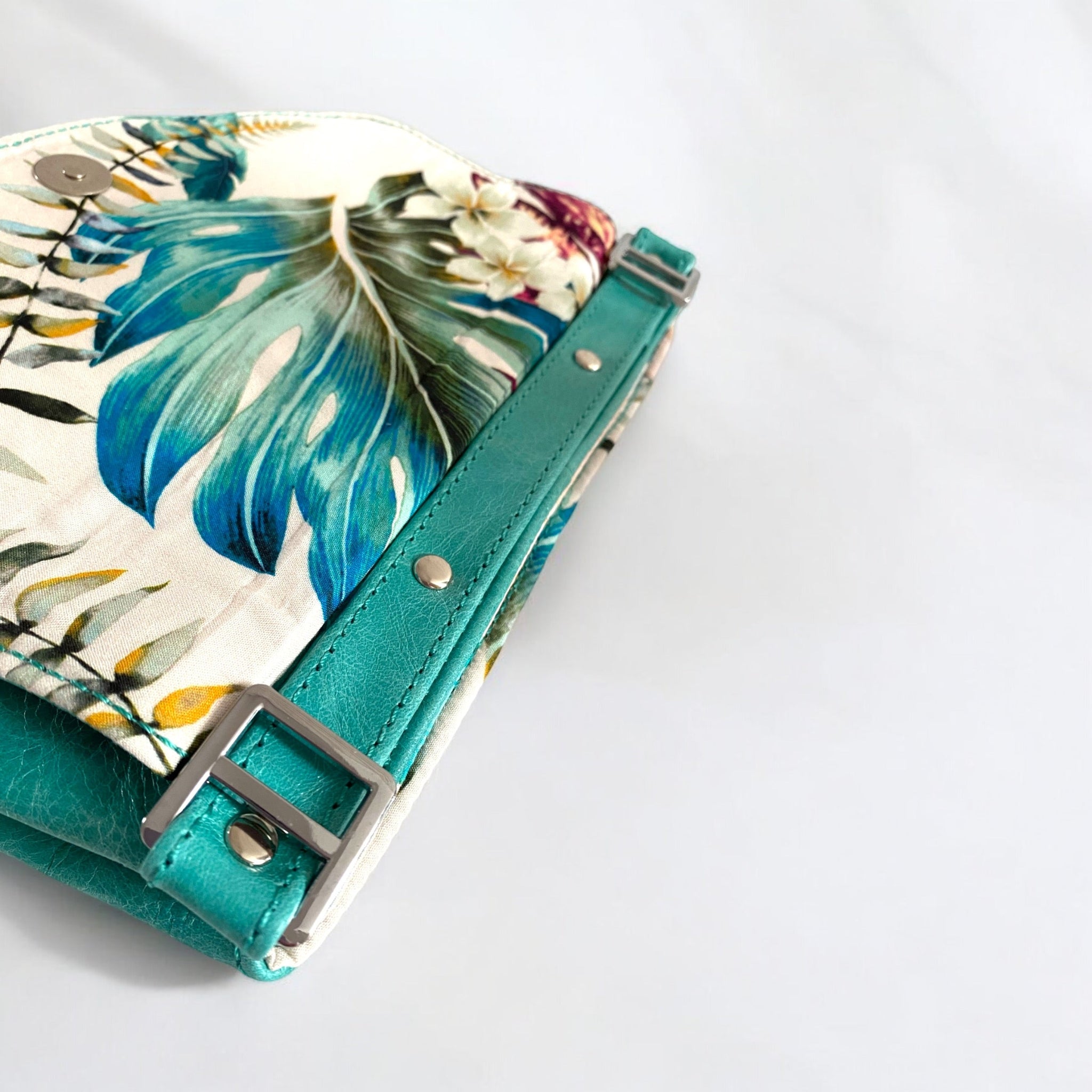 Turquoise leather crossbody bag with a tropical floral patterned lining on a white background