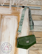 Green leather bag with a zigzag strap hanging on a wooden door.