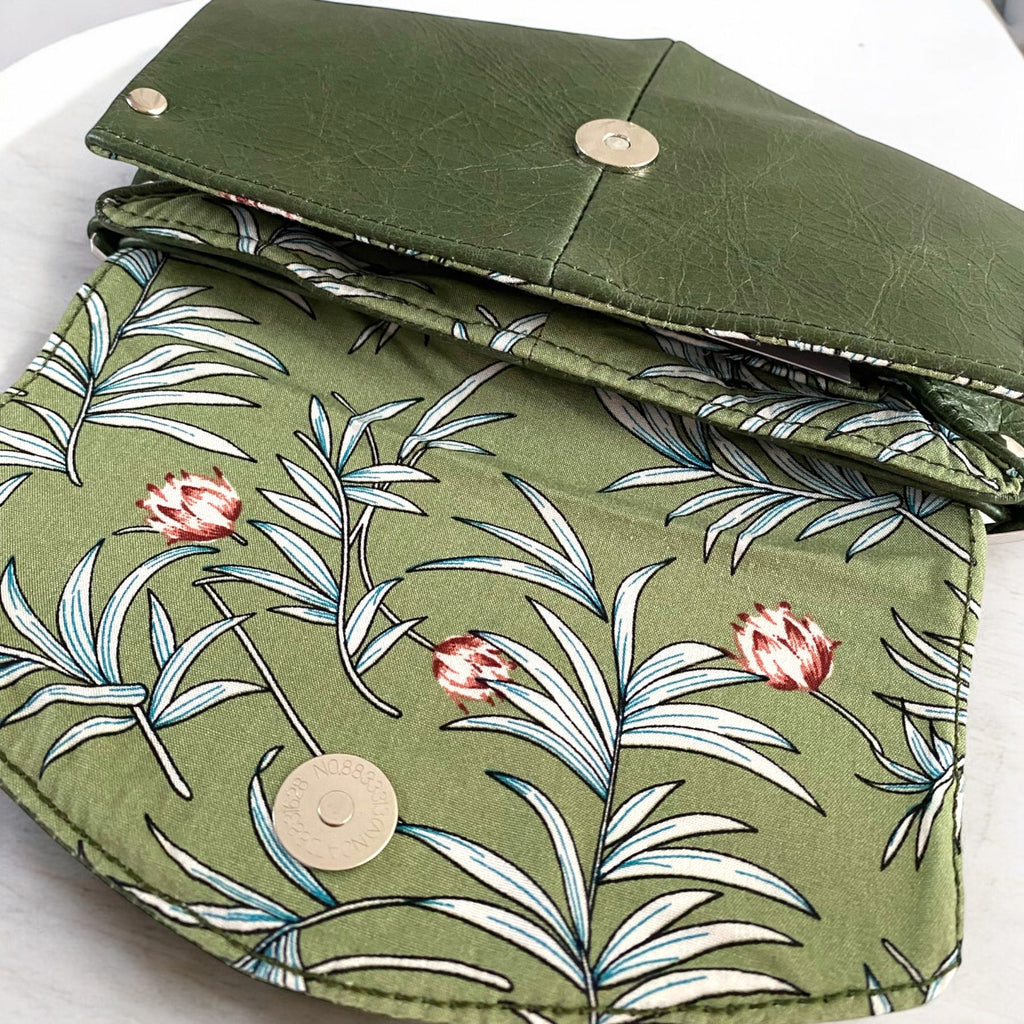 Green leather clutch bag with fan open flap to show the floral patterned fabric lining on a white background