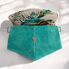 Teal leather clutch with a tropical floral interior on a light background