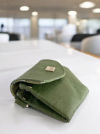 Forest green leather clutch bag on a white table in a bright room.