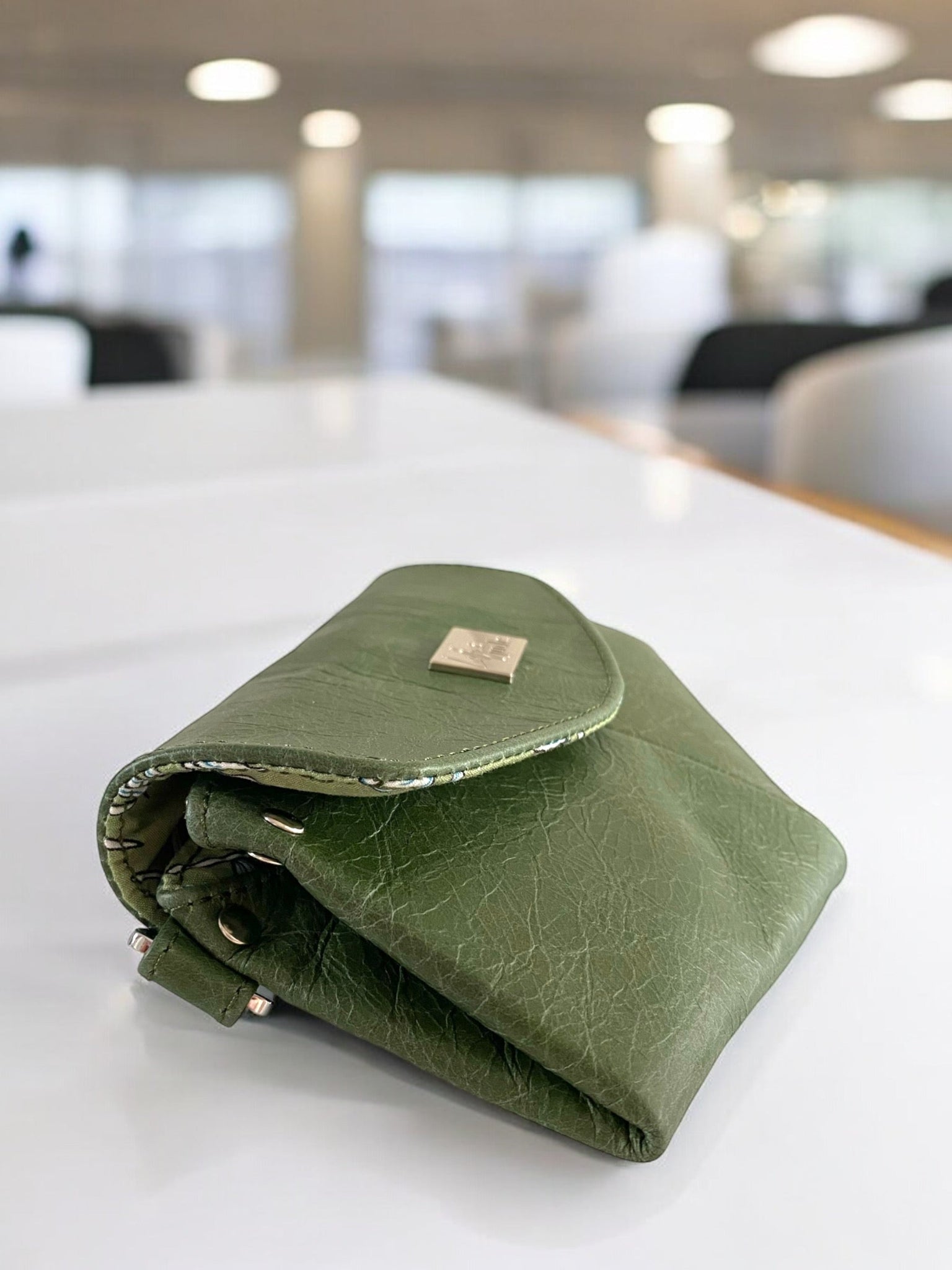 Forest green leather clutch bag on a white table in a bright room.