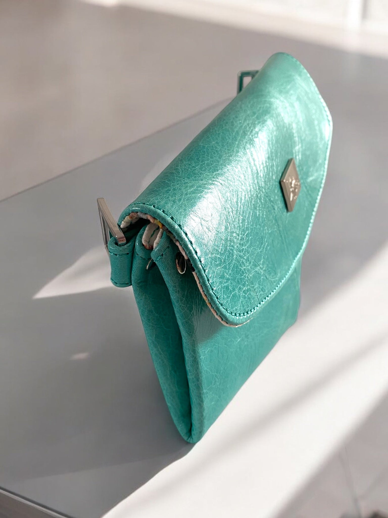 Side view of a bright turquoise leather crossbody bag with silver hardware on a white background