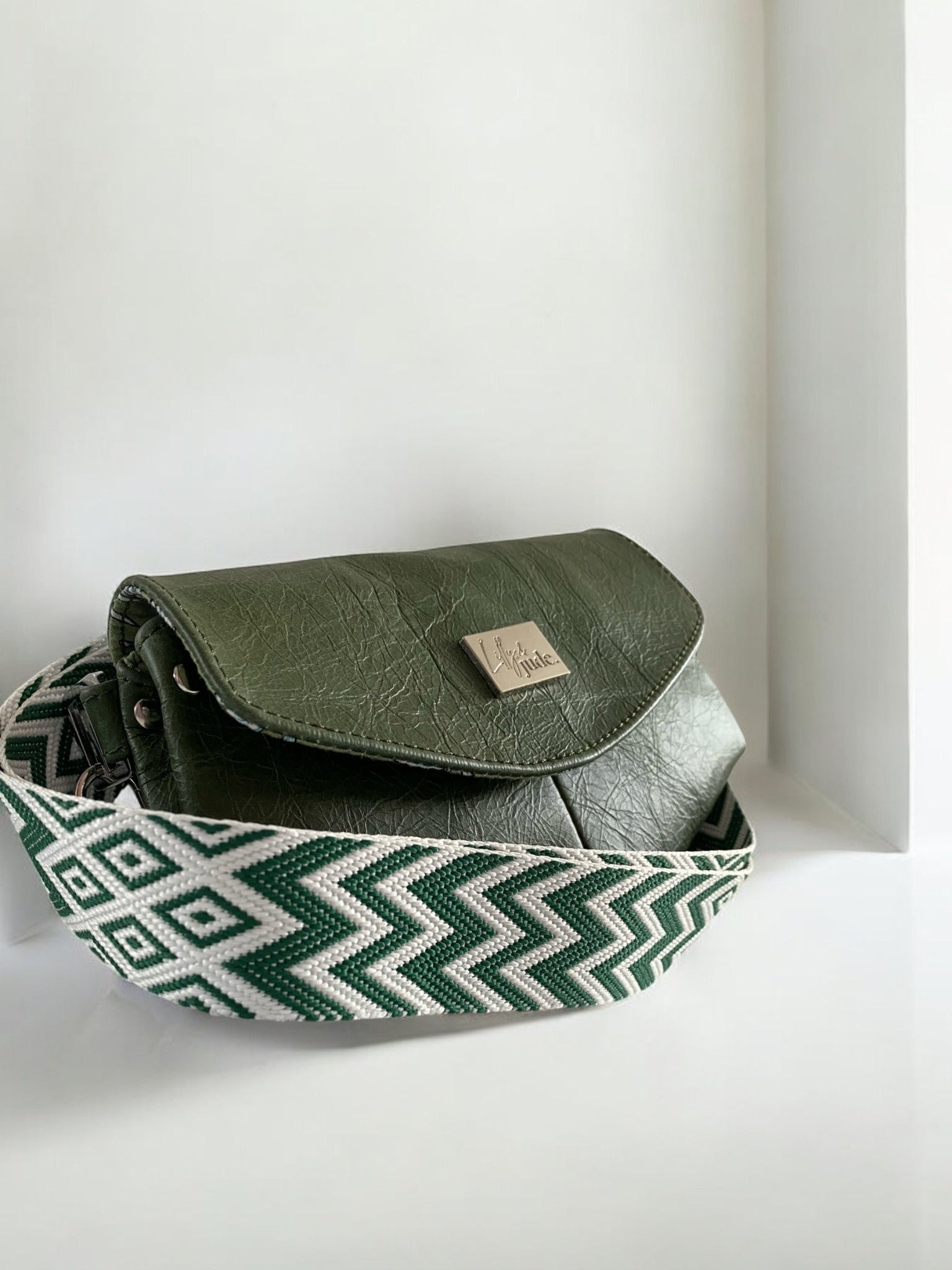 Unique, green leather bag with patterned strap on white background