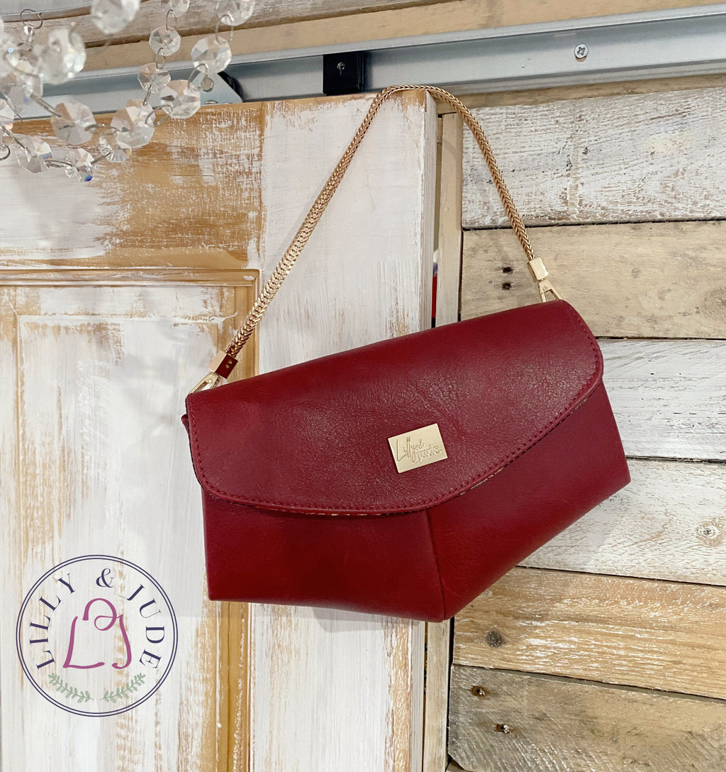 Red leather handbag with gold chain hanging on a wooden and white background